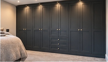 Full-height bespoke fitted bedroom wardrobes in dark charcoal with brass handles and recessed lighting by C H Joinery Solutions