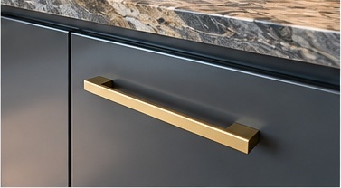 Close-up of a brushed brass cabinet handle on a graphite fitted unit beneath a marble worktop