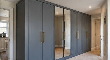 Bespoke fitted wardrobes with mirrored centre doors, blue-grey painted panels and brass handles by C H Joinery Solutions